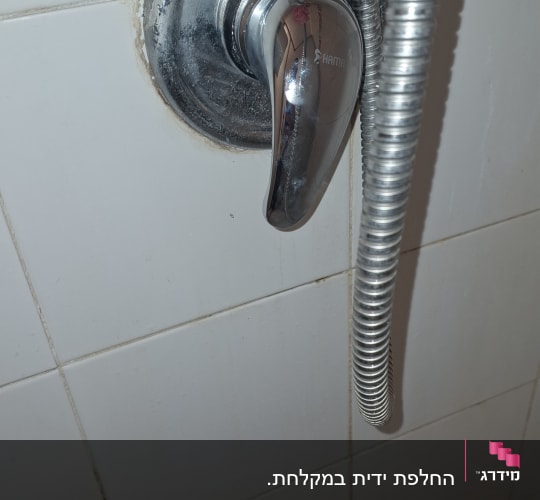 ברז מקלחת עם צינור מתכת על קיר אריחים
